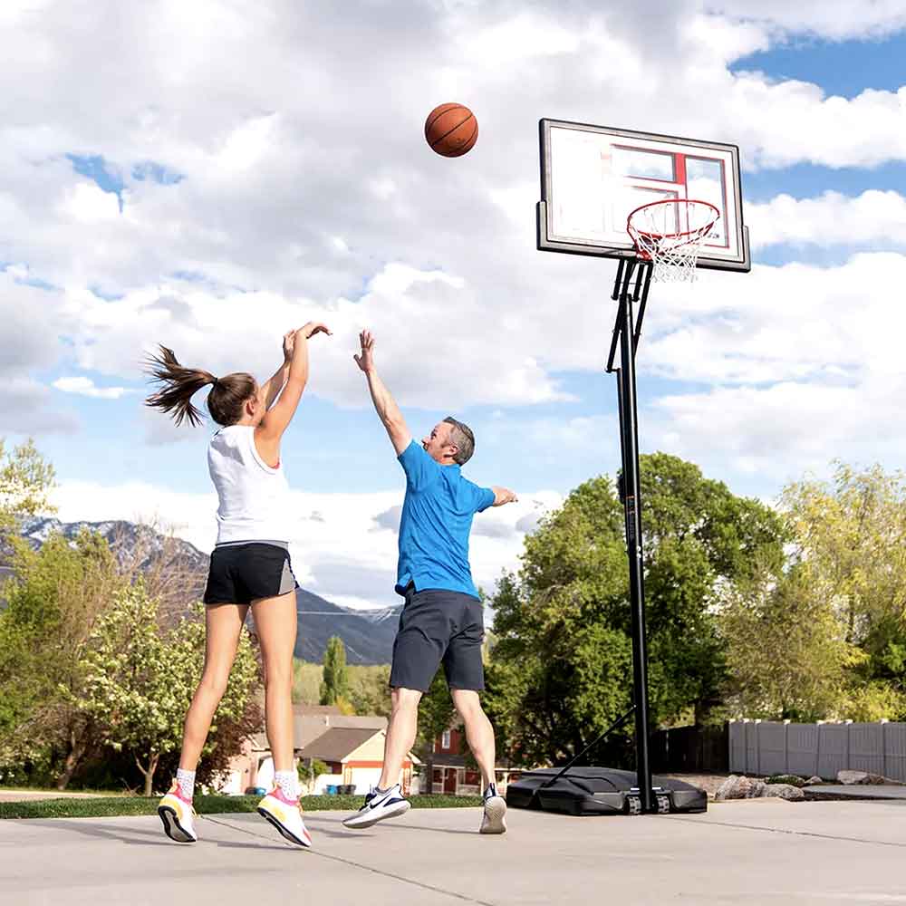 Kids playing on the tall portable basketball hoop in a sunny backyard