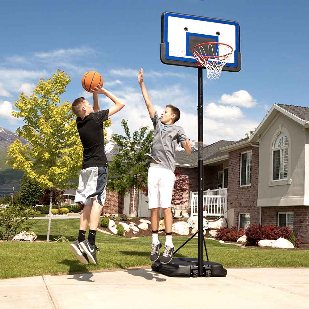 Two boys playing on the portable hoop in front of a house