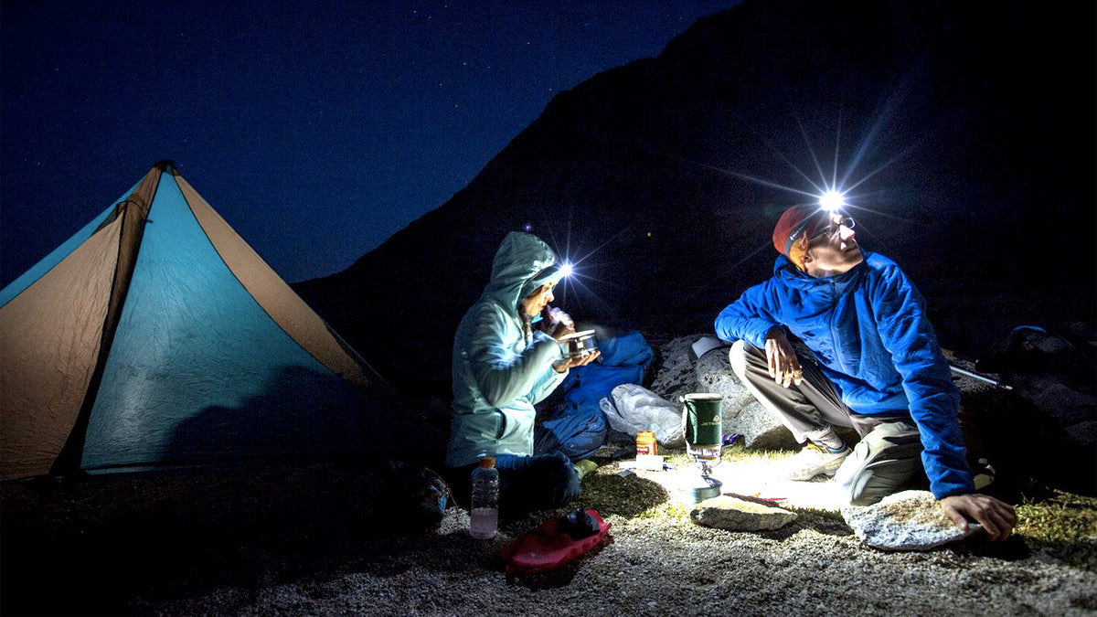 Campers by a tent at night, lit by a headlamp