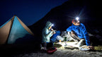 Campers by a tent at night, lit by a headlamp