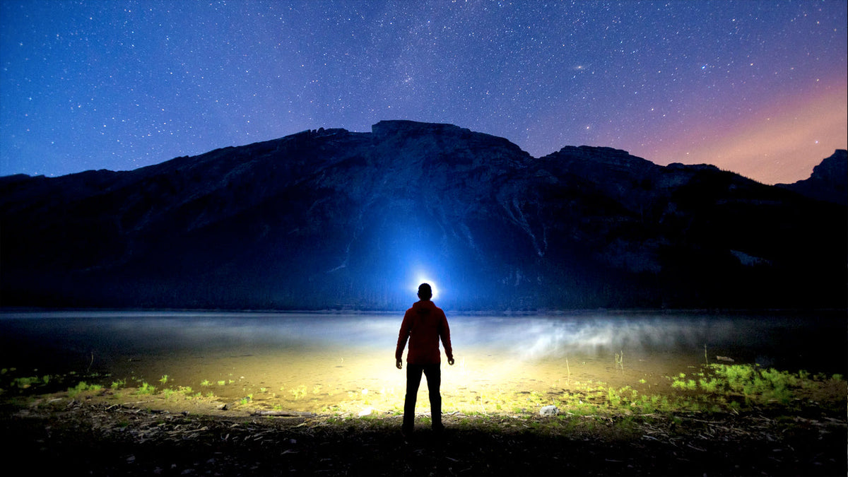 Person on a hilltop at night with a long headlamp beam