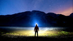 Person on a hilltop at night with a long headlamp beam