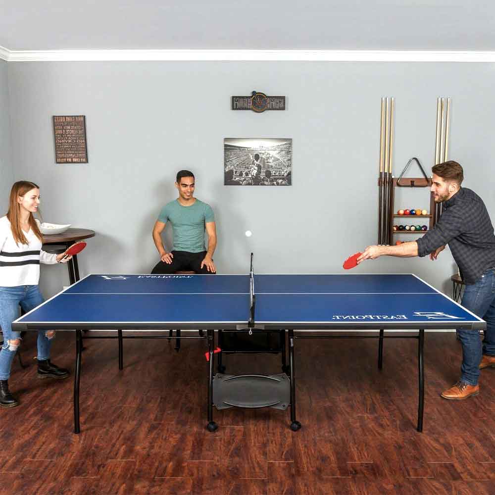 Friends playing ping pong on the blue table in a living room