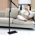 Woman relaxing on a sofa with a tablet held by the black floor stand