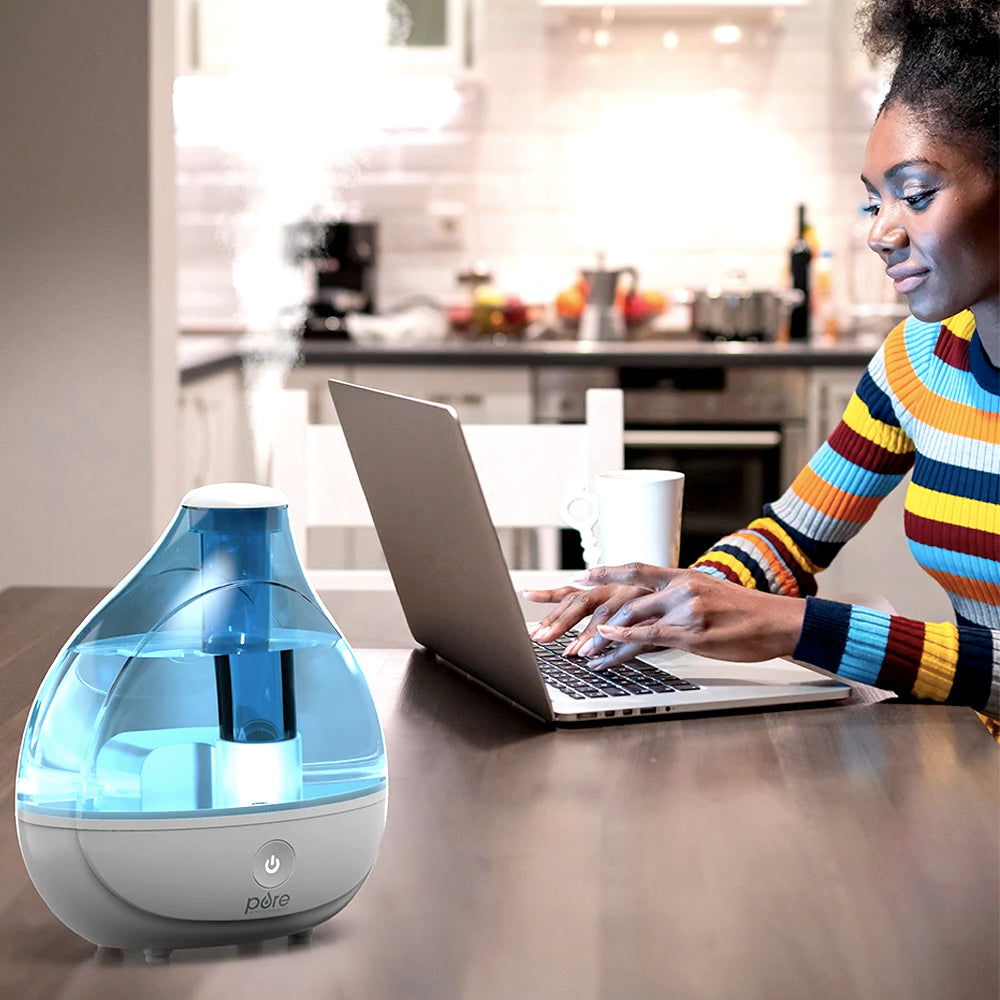 Blue cool mist humidifier on a table beside a woman working on a laptop