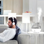 Clear cool mist humidifier beside a man relaxing on a sofa