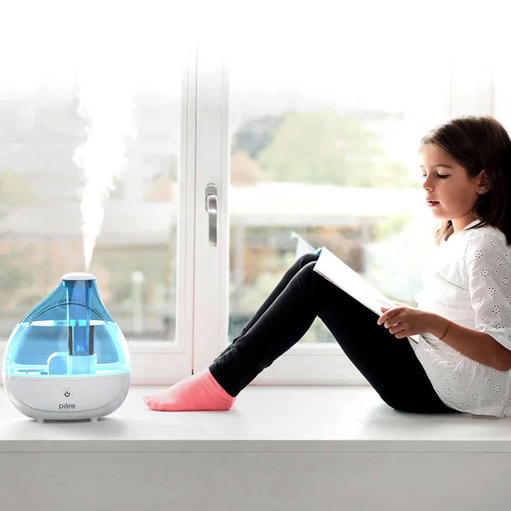 Blue humidifier misting by a window as a girl reads